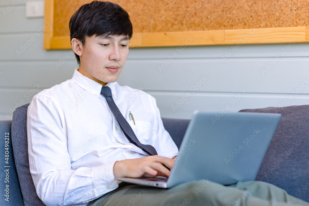 Asian thoughtful young handsome professional successful male businessman employee in formal business outfit sitting on cozy sofa couch thinking ideas working with laptop computer in living room Asian thoughtful young handsome professional successful male businessman employee in formal business outfit sitting on cozy sofa couch thinking ideas working with laptop computer in living room