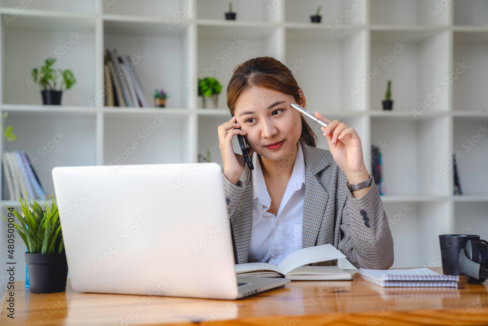 business woman at work talking on phone and taking notes, sitting at her working place in office, copy space