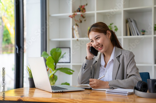 business woman at work talking on phone and taking notes, sitting at her working place in office, copy space