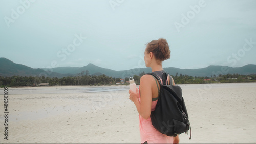 Person in sportwear with bottle in hand walk on tropical beach
