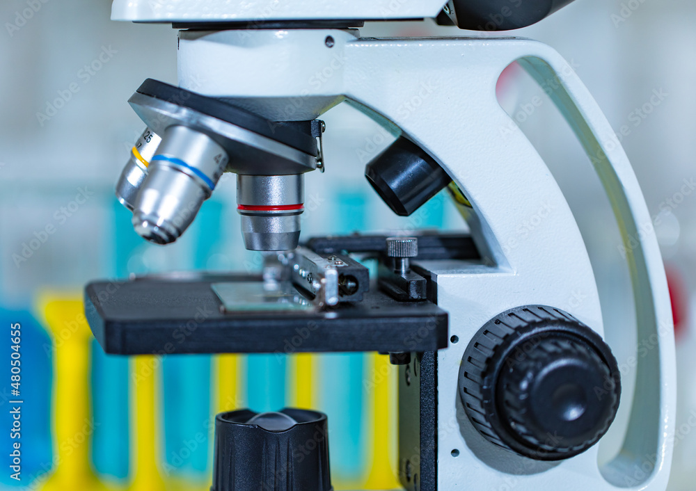 Fototapeta premium Closeup studio shot of magnifier zooming lens microscope camera placing on working table in hospital laboratory full of glassware equipment test tube rack Erlenmeyer flask beaker and computer monitor