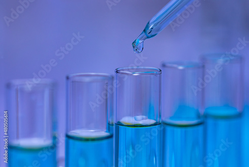 Closeup studio shot of scientific lab glass dropper dropping blue reagent solvent solution liquid sample into glassware test tube line in rack for analyzing science experiment in hospital laboratory