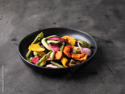 Dehydrated vegan chips in a wooden mango bowl. Vitamin healthy fast food with carrot slices, beetroot wedges, broccoli, zucchini on a light table. food photo banner copy space.