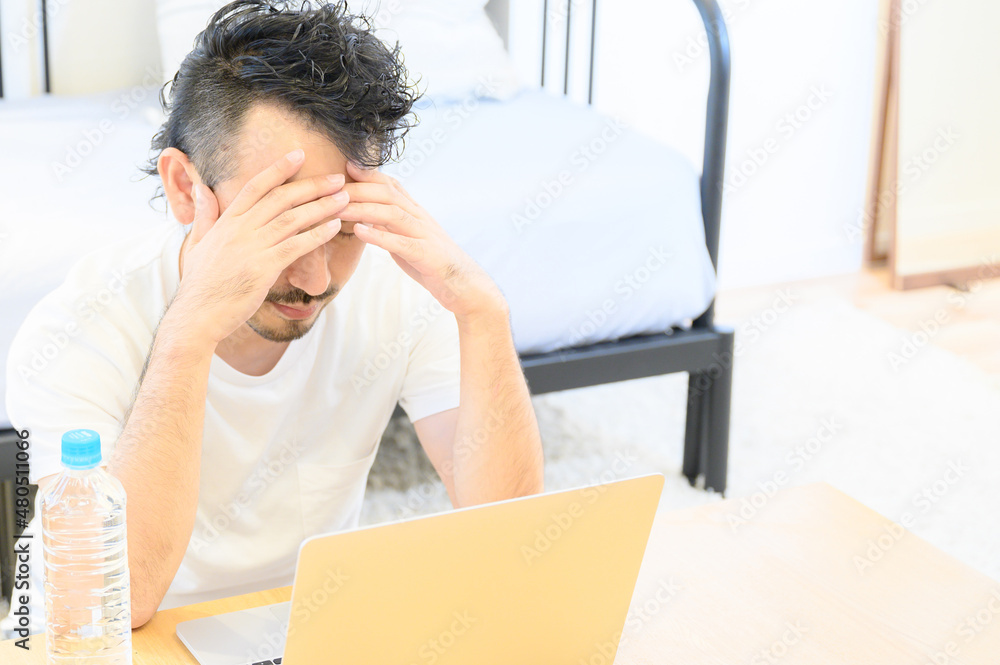 A middle-aged Asian man struggling with his head in front of his computer. A middle-aged Asian man struggling with his head in front of his computer.