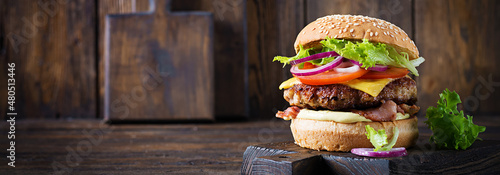 Hamburger with bacon, turkey burger meat, cheese, tomato and lettuce on wooden background. Tasty burger. Close up