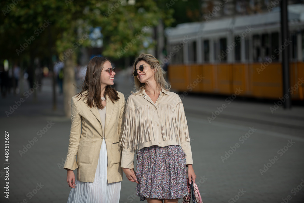 Two excited happy women walking together on the street. Happy fashionable girls in city. Young joyful women expressing positivity, vacation with cheerful emotions, great mood.