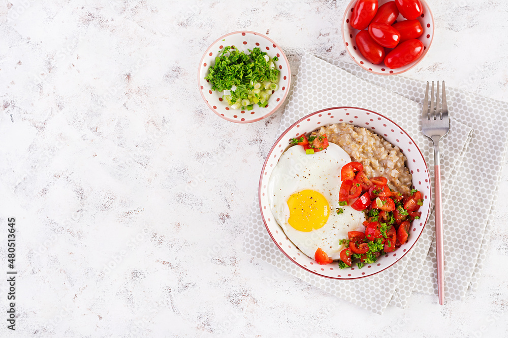 Breakfast oatmeal porridge with roasted egg and tomatoes salad. Healthy balanced food. Top view, above Breakfast oatmeal porridge with roasted egg and tomatoes salad. Healthy balanced food. Top view, above