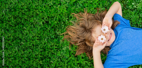 Banner with spring child face. Happy child lying on green grass outdoors in spring park. Kids on green grass background.