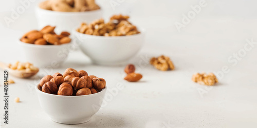 Hazelnuts and other nuts in white bowls on a white background. Banner