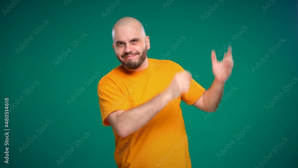 Bald middle-aged man with a beard in an orange t-shirt points with his hand to the up and right on a green background Bald middle-aged man with a beard in an orange t-shirt points with his hand to the up and right on a green background