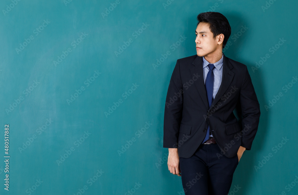 Portrait studio shot of Asian young professional successful male teacher in black formal suit and necktie standing smiling look at camera in front green blackboard background in classroom at school Portrait studio shot of Asian young professional successful male teacher in black formal suit and necktie standing smiling look at camera in front green blackboard background in classroom at school