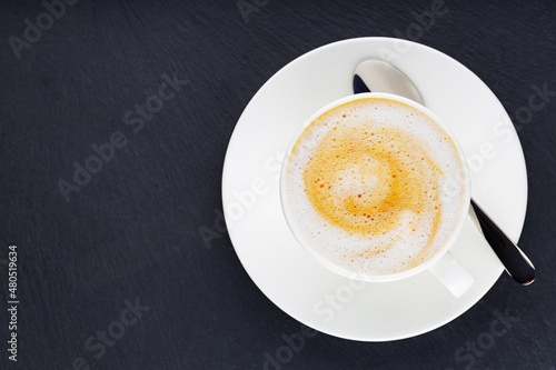 Cup of coffee on a dark background. Coffee on a slate board. Cup of morning coffee on a white saucer. Top view. Copy space