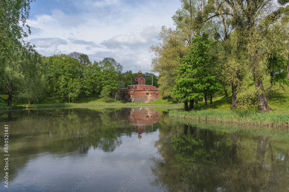 Fototapeta premium parks pond on spring day with small brick chapel afar