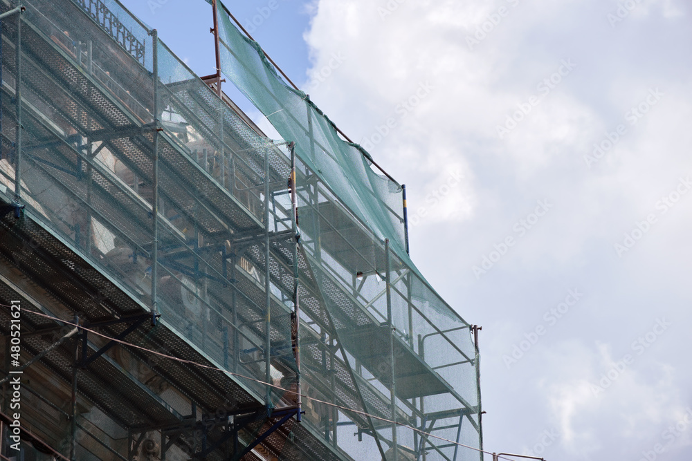 Building facade under renovation works with construction scaffolding frame covered with protective net for workers safety Building facade under renovation works with construction scaffolding frame covered with protective net for workers safety