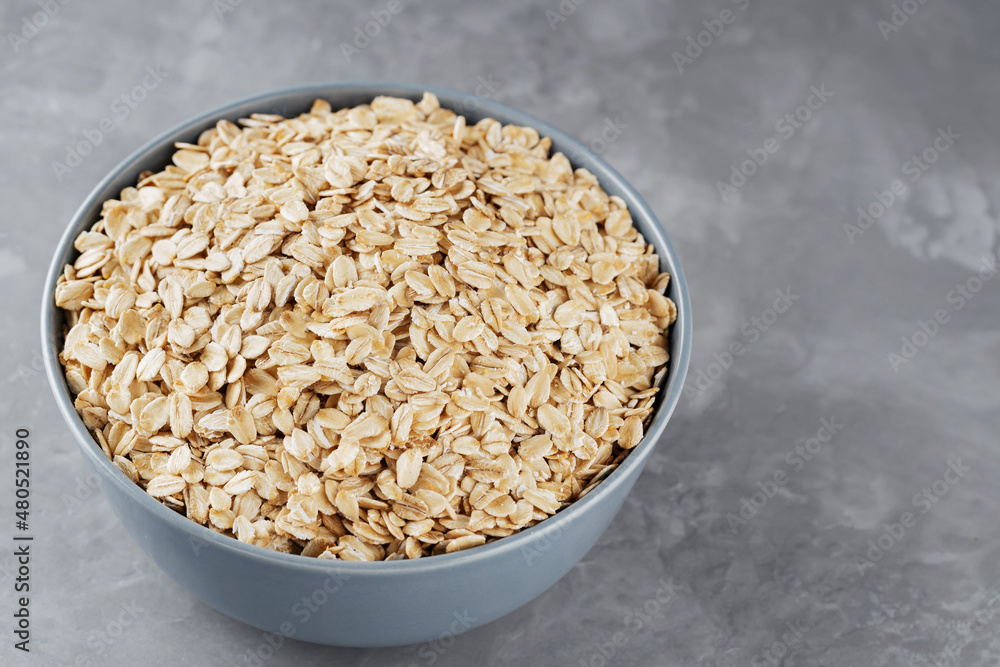 Bowl of oat flakes on gray background. Dry rolled oats in a gray bowl. Raw oatmeal flakes. Copy space. Top view Bowl of oat flakes on gray background. Dry rolled oats in a gray bowl. Raw oatmeal flakes. Copy space. Top view