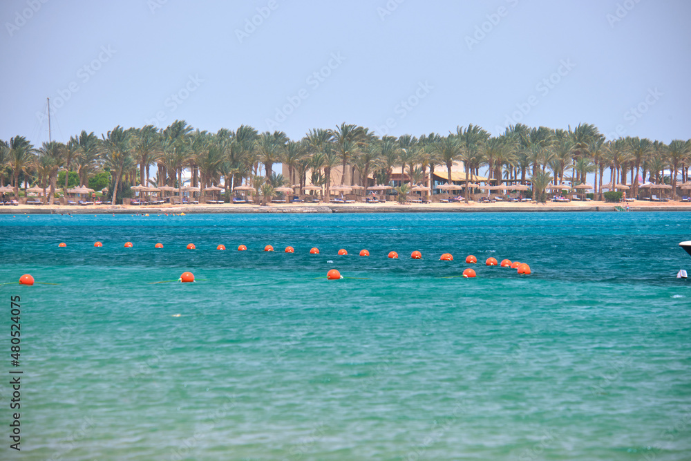 Yellow buoys floating on sea surface as marker for swimming restriction in deep water at tropical resort with view of coast line in distance. Human life safety concept