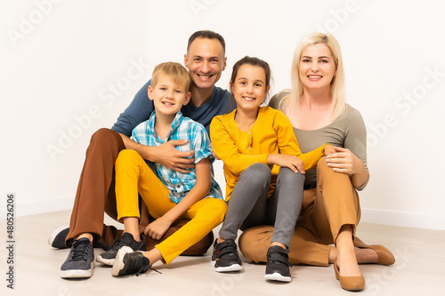 Portrait of the happy family with two children sitting at studio on white floor