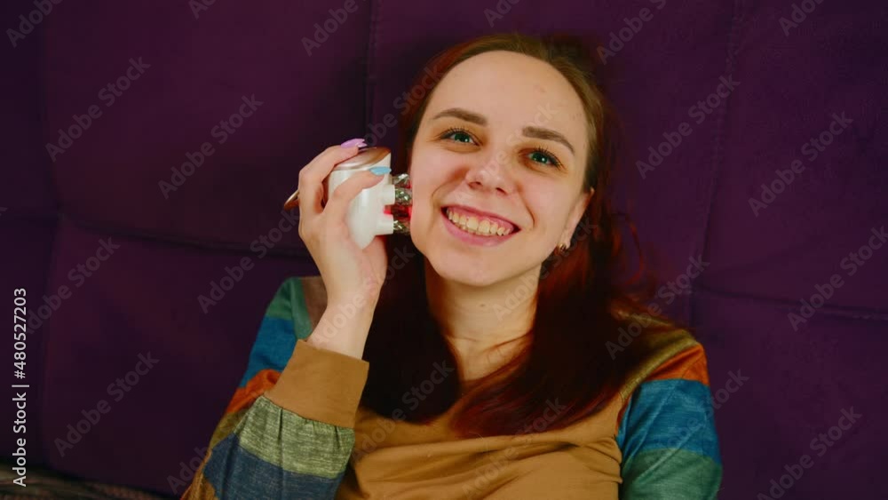 Cheerful woman using face massager. From above of content female using electric massager on face while relaxing on sofa and doing beauty procedure at home Cheerful woman using face massager. From above of content female using electric massager on face while relaxing on sofa and doing beauty procedure at home
