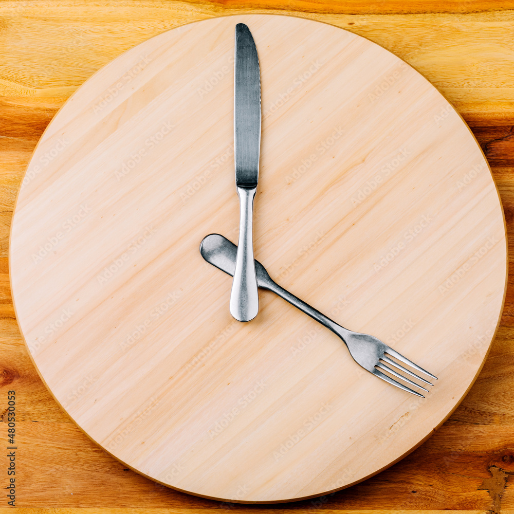 The concept of intermittent fasting and skipping meals. Wooden round tray with cutlery in the form of clock hands The concept of intermittent fasting and skipping meals. Wooden round tray with cutlery in the form of clock hands