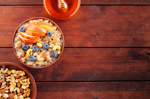 Oatmeal porridge with blueberries, apple slices and nuts on a wooden boards. Oatmeal, various nuts, and honey for a healthy breakfast. Top view. Copy space