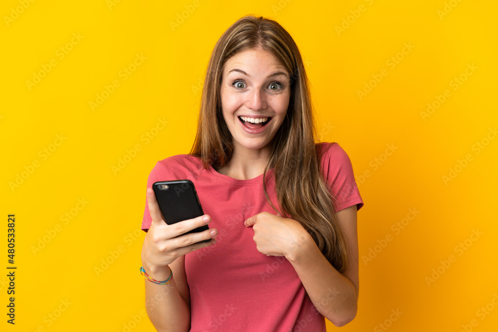 Young woman using mobile phone isolated on yellow background with surprise facial expression Young woman using mobile phone isolated on yellow background with surprise facial expression