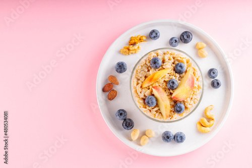 Oatmeal cereal with apples and blueberries on a pink background. Healthy breakfast with oatmeal, nuts and berries on white plate. Top view. Copy space