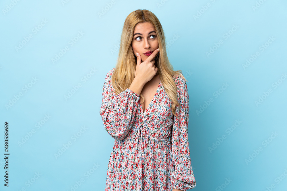 Young Uruguayan blonde woman over isolated blue background having doubts and with confuse face expression Young Uruguayan blonde woman over isolated blue background having doubts and with confuse face expression