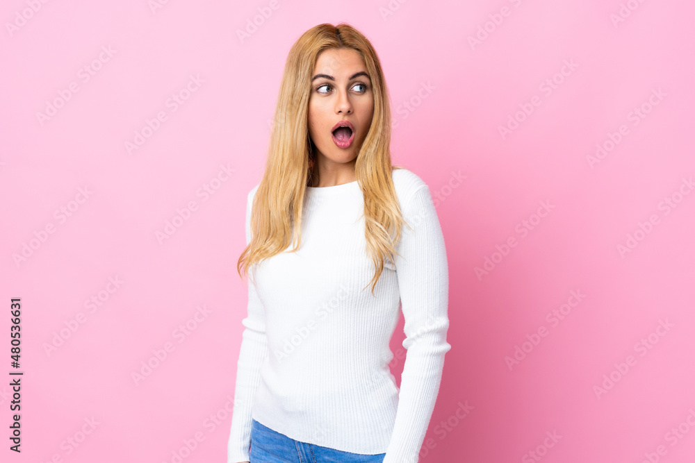 Young Uruguayan blonde woman over isolated pink background doing surprise gesture while looking to the side Young Uruguayan blonde woman over isolated pink background doing surprise gesture while looking to the side