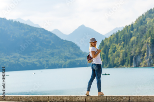 Photography Beautiful tourist lady wearing hat and backpack enjoying stunning view on Bavarian mountains near Neuschwanstein castle in Germany