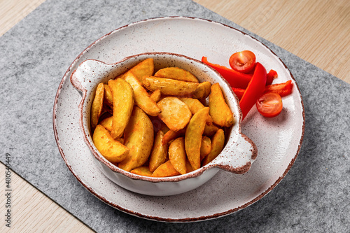 A bowl of crispy baked potato wedges, red pepper and cherry tomato, close-up