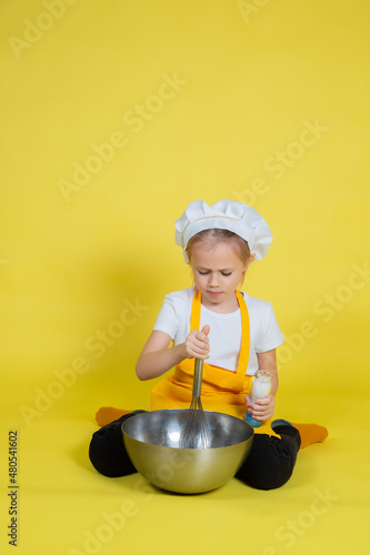 Girl in apron and chef's hat sitting on the floor with a bowl and whisk