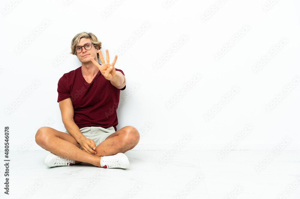 Young English man sitting on the floor happy and counting four with fingers Young English man sitting on the floor happy and counting four with fingers