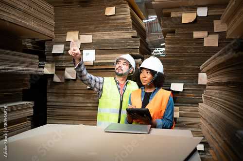 Принти на полотні Two Asian warehouse workers standing among the stack of flat pack cardboard boxes, man with beard counting the stock to woman who recording on tablet while doing a stocktaking together in warehouse