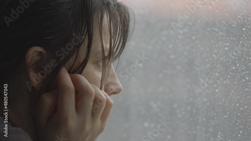 Sad woman watching the rain at the window