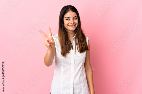 Young caucasian woman isolated on pink background smiling and showing victory sign © luismolinero