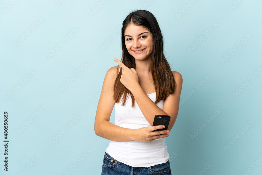 Young caucasian woman using mobile phone isolated on blue background pointing to the side to present a product Young caucasian woman using mobile phone isolated on blue background pointing to the side to present a product