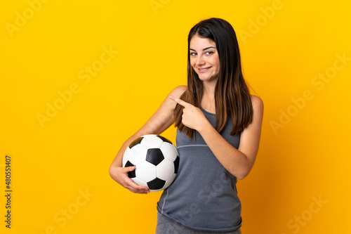 Young football player woman isolated on yellow background pointing to the side to present a product © luismolinero