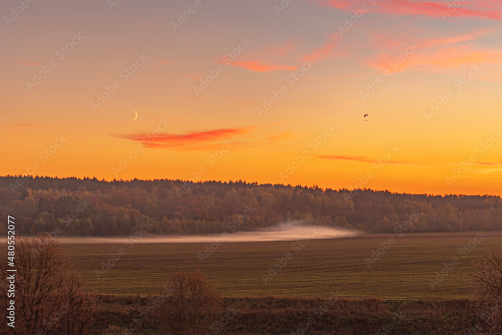 Sunset in the mist field with silhouette of paragliders flying over the orange sky