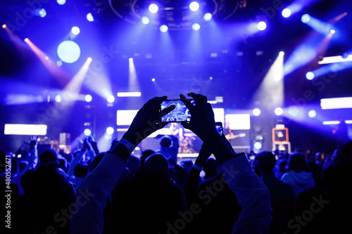 Hands with a smartphone at the concert hall during music and light show.