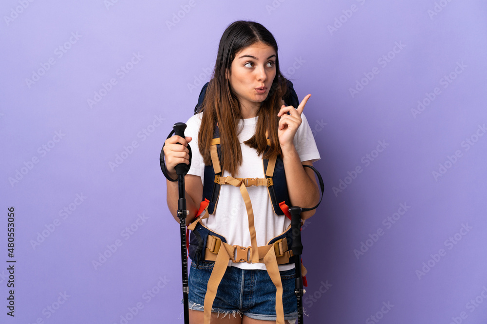 Young woman with backpack and trekking poles isolated on purple background thinking an idea pointing the finger up Young woman with backpack and trekking poles isolated on purple background thinking an idea pointing the finger up
