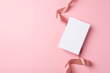 Top view photo of saint valentine's day decorations curly silk ribbon and paper card on isolated pastel pink background with copyspace