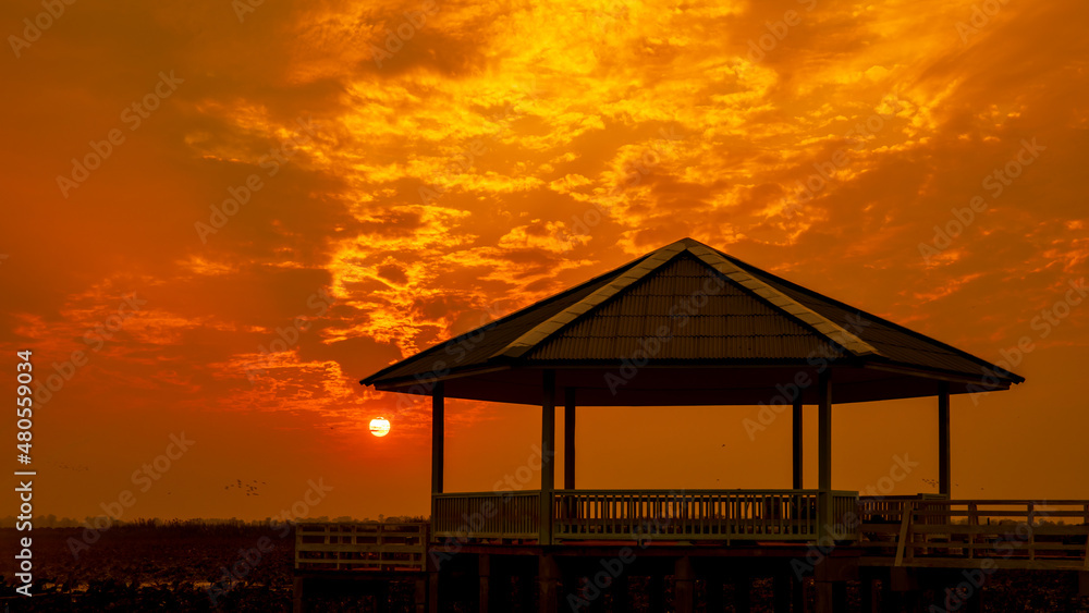 Fototapeta premium Vintage Wooden Pavilion is under construction with light from sunset or evening time at water lake of public park of Bueng See Fai, Phichit Province, Thailand.