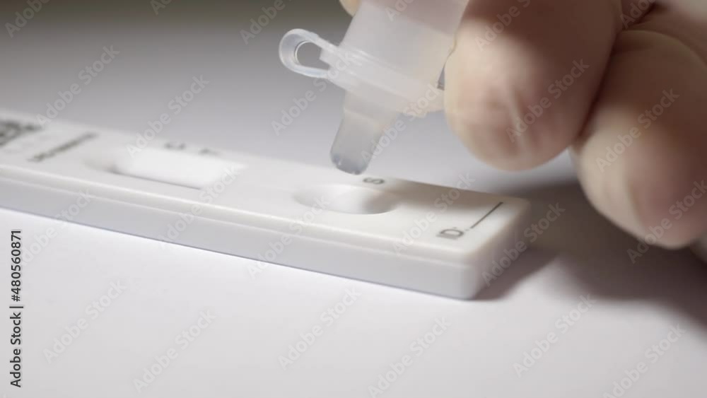 A home lateral flow test. Close-up using the dropper tube and squeezing 4 drops of liquid into the specimen well on the test cassette. During Covid-19 pandemic. A home lateral flow test. Close-up using the dropper tube and squeezing 4 drops of liquid into the specimen well on the test cassette. During Covid-19 pandemic.