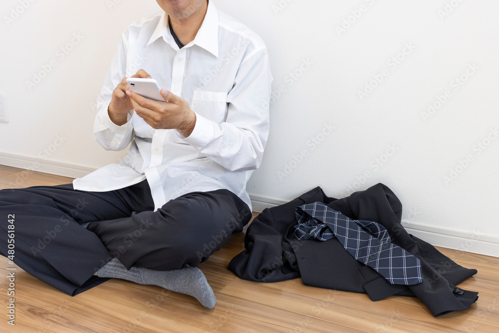 スーツを脱いでリラックスしてスマートフォンを使う男性 スーツを脱いでリラックスしてスマートフォンを使う男性