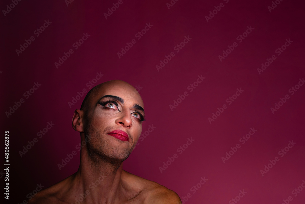 Beautiful transgender gay man wearing makeup looking up, isolated on pink background; with copyspace Beautiful transgender gay man wearing makeup looking up, isolated on pink background; with copyspace