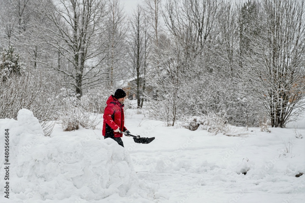 man in a red jacket cleans the road from snow with a shovel in the village