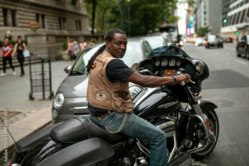 Cool handsome middle aged afro American man sitting on a Harley motorbike (motorcycle) on the street on Manhattan. New York. Wearing jeans and black t-shirt. Smiling and positive. Relaxed. © Chiralli