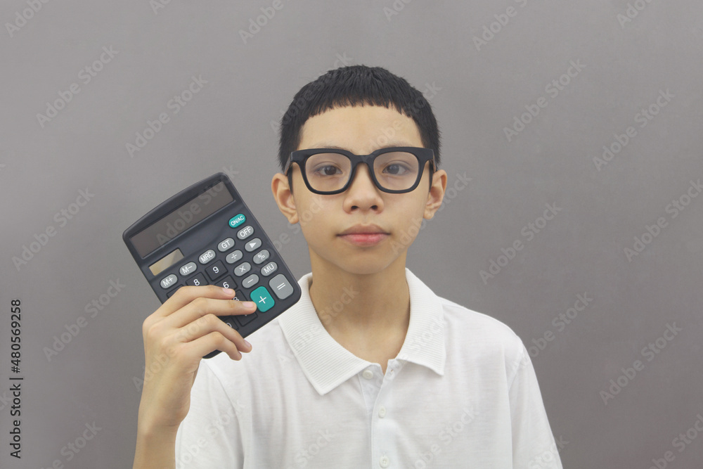 Cute and friendly Asian boy in glasses holding calculator on gray background. Cute and friendly Asian boy in glasses holding calculator on gray background.