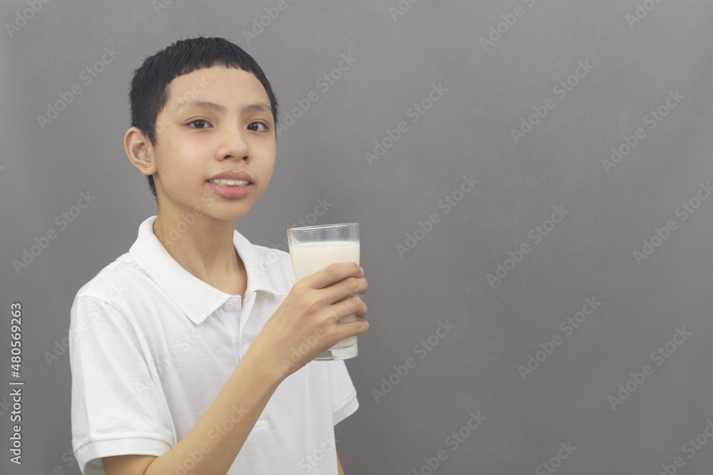 Friendly Asian boy holding glass of milk on gray background. Copy space for text. Friendly Asian boy holding glass of milk on gray background. Copy space for text.