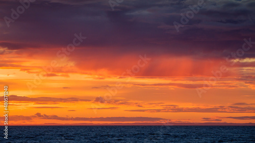 Dramatic orange cloudscape over deep blue water at sunset